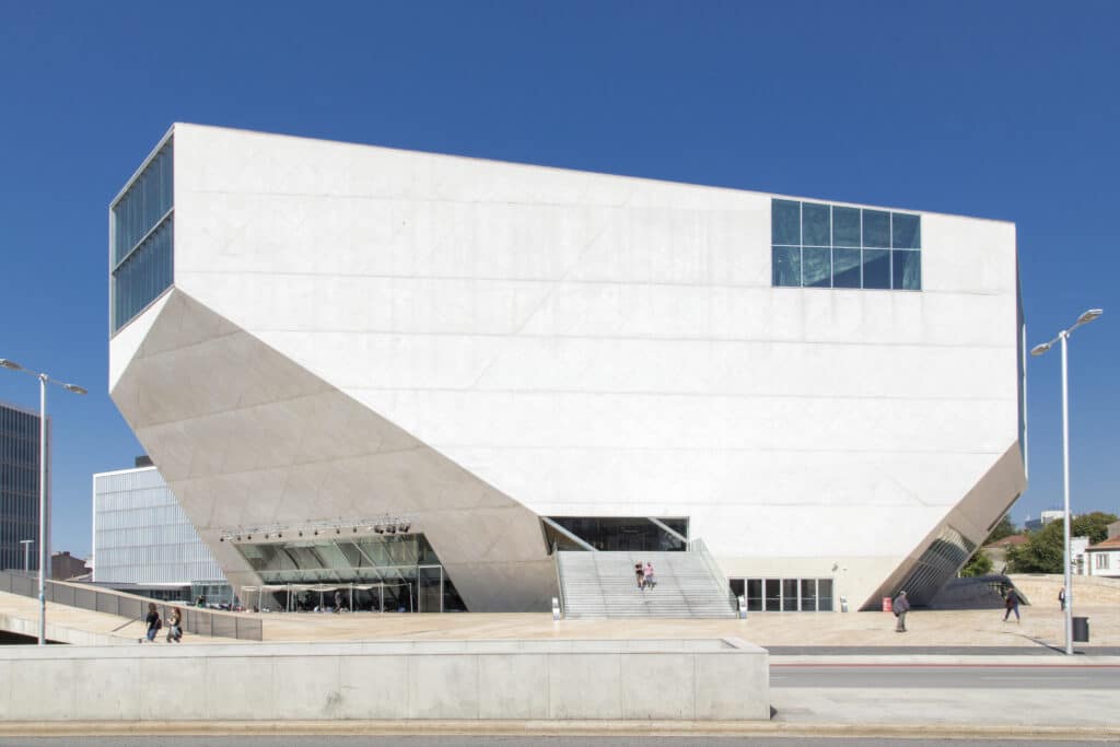 A Casa da Música, um edifício geométrico branco e moderno no Porto, com grandes janelas e uma entrada pública, frente a um céu azul claro.