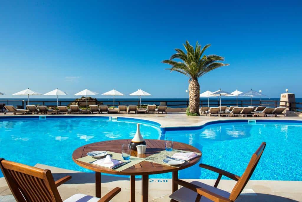 Piscina exterior do Vilalara Thalassa Resort, com mesa e cadeiras em primeiro plano.