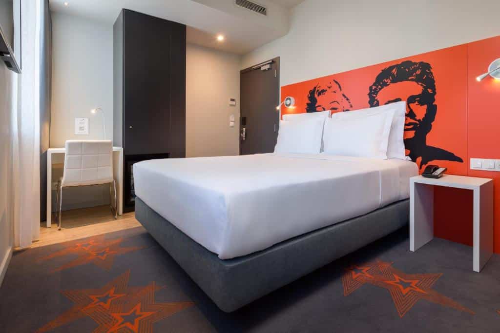 Quarto do Star Inn Lisbon Airport com cama de casal, um armário de uma porta, uma pequena mesa com cadeira ao lado e, em frente à cama, uma janela e uma televisão