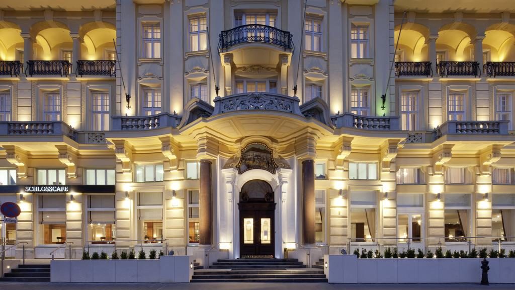 Grande entrada de um edifício histórico e ornamentado do Austria Trend Parkhotel Schönbrunn Wien, com uma porta em arco e a fachada iluminada à noite.