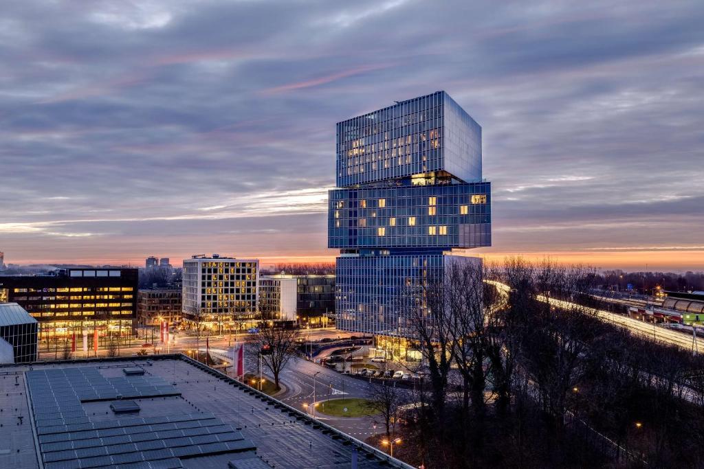 Edifício do nhow Amsterdam Rai, com a forma de três triângulos sobrepostos em direções diferentes, iluminado ao início da noite