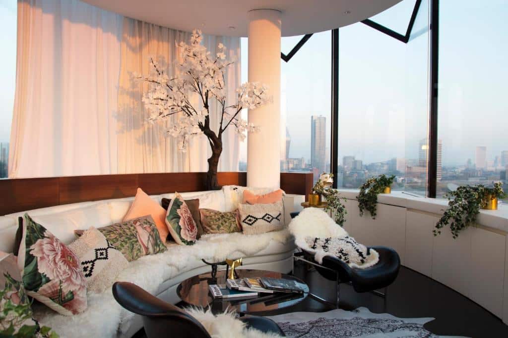 Varanda fechada e ampla do ME London by Melia com janelas panorâmicas e um sofá cheio de almofadas