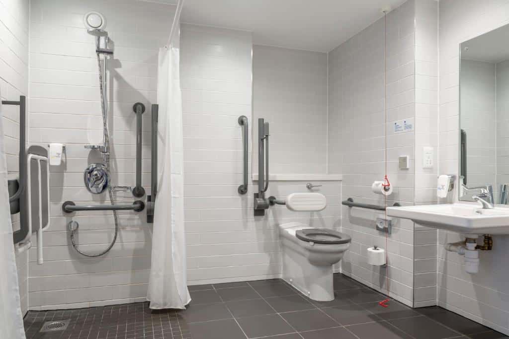 Casa de banho acessível do Holiday Inn Express Dublin City Centre com azulejos claros, chuveiro embutido, barras de apoio e sanita com assento elevado.
