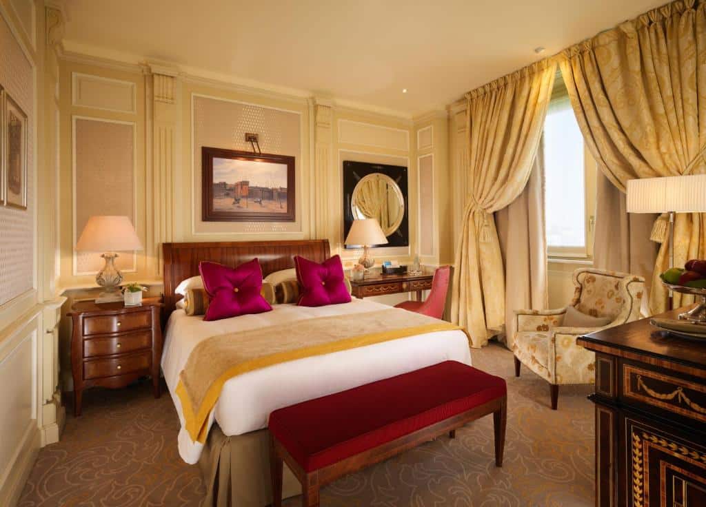 Quarto requintado em tons de dourado e vermelho, com cortinados, cama de casal e mobiliário em madeira no Hotel Principe Di Savoia