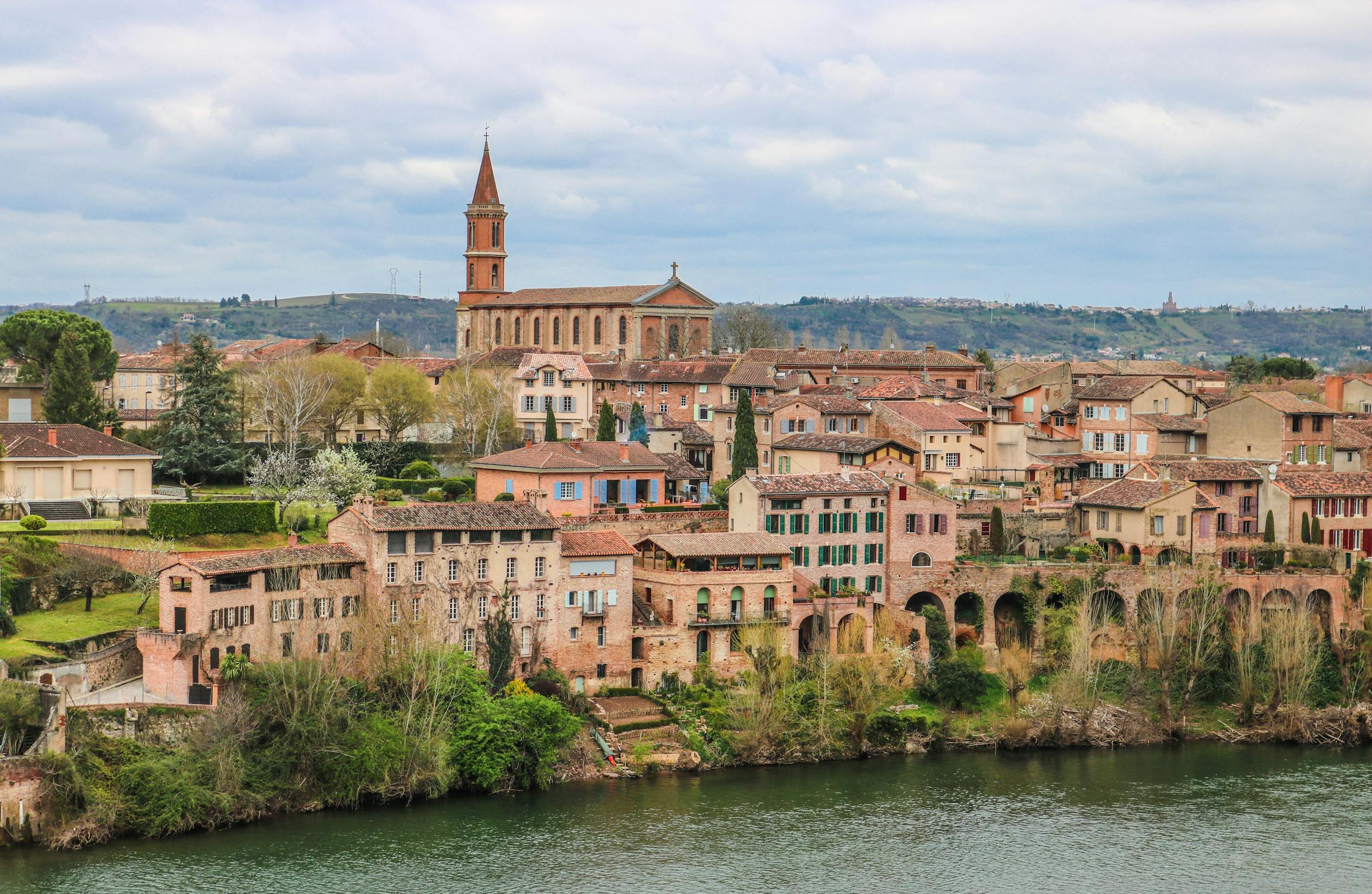 Vista panorâmica de Albi, com edifícios históricos, uma igreja de torre alta e um rio em primeiro plano.