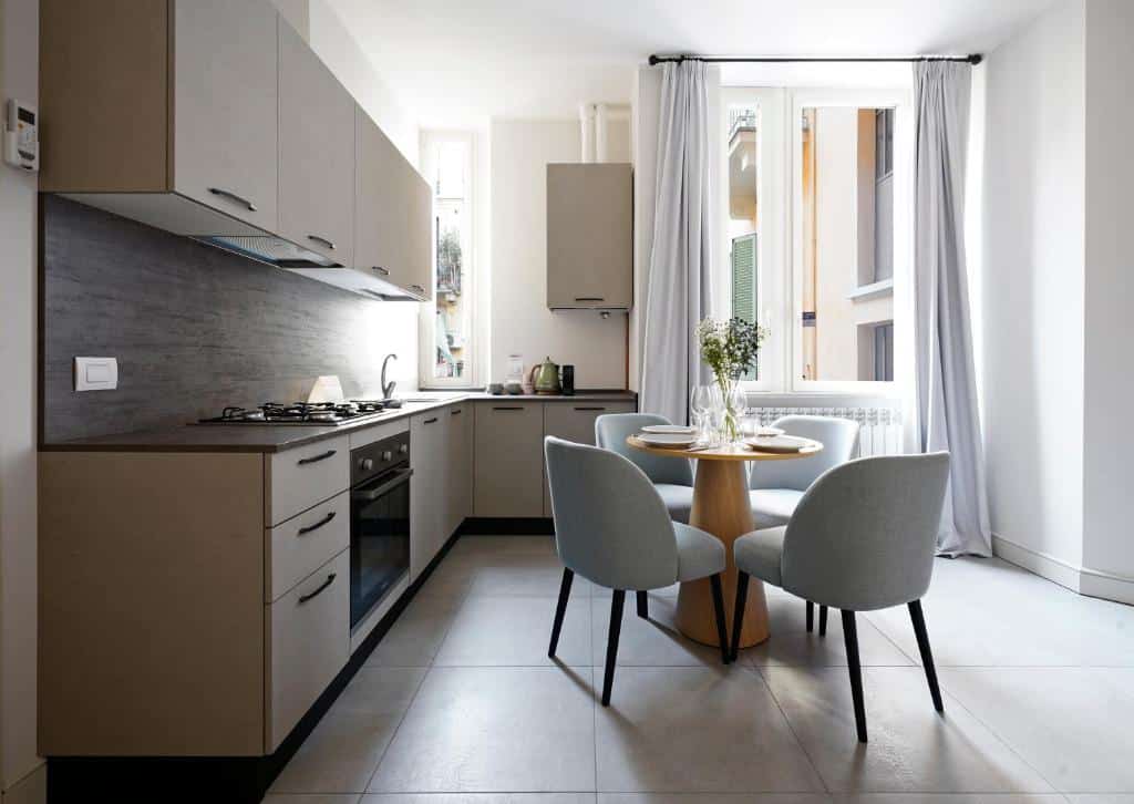 Cozinha do numa I Loreto Apartments com uma janela com cortinas, uma pequena mesa com quatro cadeiras estofadas e uma cozinha com fogão, forno, armários e lava-loiça