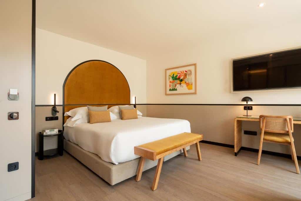 Quarto do The Editory Garden Porto Hotel com cama de casal, banco de madeira aos pés da cama e secretária com televisão.
