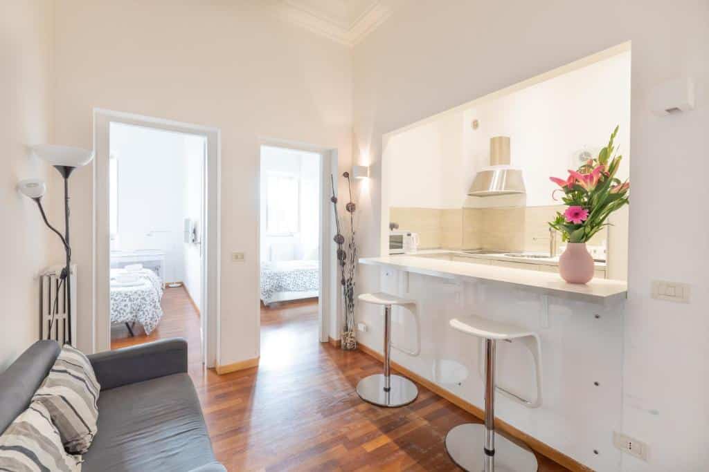 sala do Stay In Rome com sofá e cozinha americana em frente, duas cadeiras altas e equipamento de cozinha, com duas portas que dão para os dois quartos do apartamento