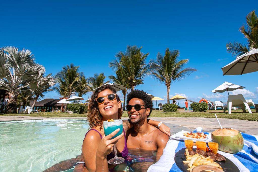 Casal sorrindo em jacuzzi com coquetel azul e petiscos em resort de praia paradisíaca