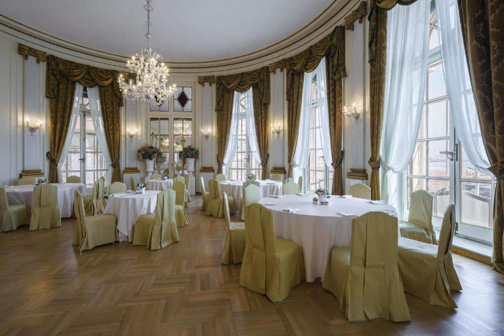 Salão elegante com decoração luxuosa do Eurostars Hotel Excelsior, com cortinas douradas, lustre de cristal e mesas com toalhas e arranjos florais, preparado para um evento formal.