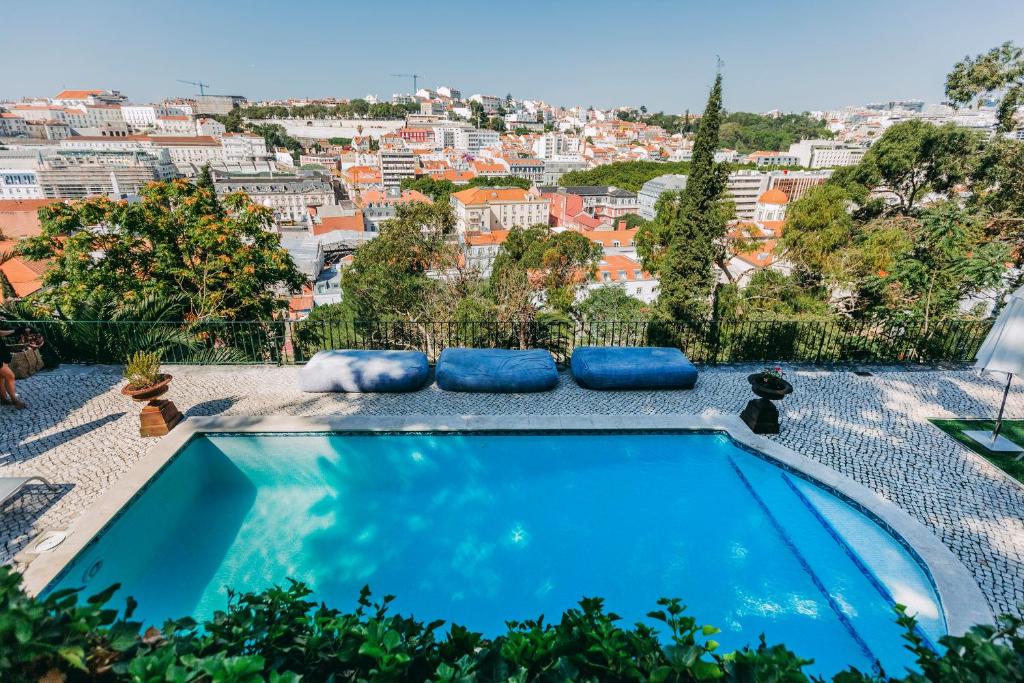 Piscina do Torel Palace Lisbon com vista direta para a cidade e algumas almofadas grandes no deck junto à piscina