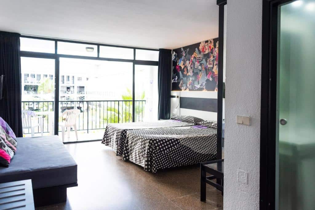 Quarto do Ibiza Rocks Hotel com duas camas, colchas de bolinhas, arte na parede, sofá e varanda com grandes janelas.