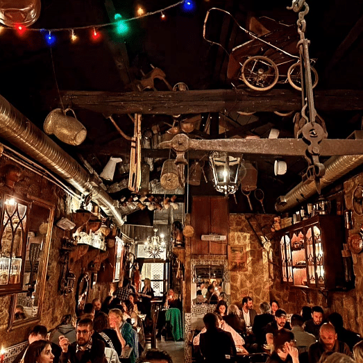 Restaurante rústico do Museu D'Avó com luz suave, vários objetos vintage pendurados no teto e nas paredes; clientes a jantar em várias mesas.