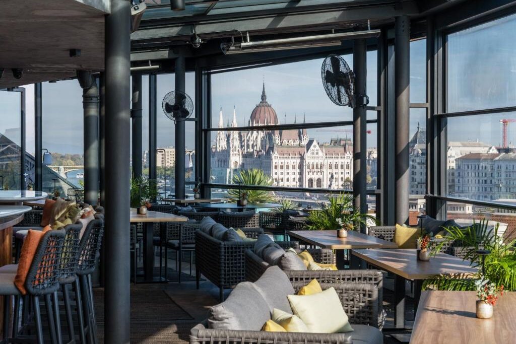 Restaurante moderno do Hotel Clark na cobertura, com lugares almofadados, mesas de madeira e vista da cidade, com um edifício abobadado ao longe.