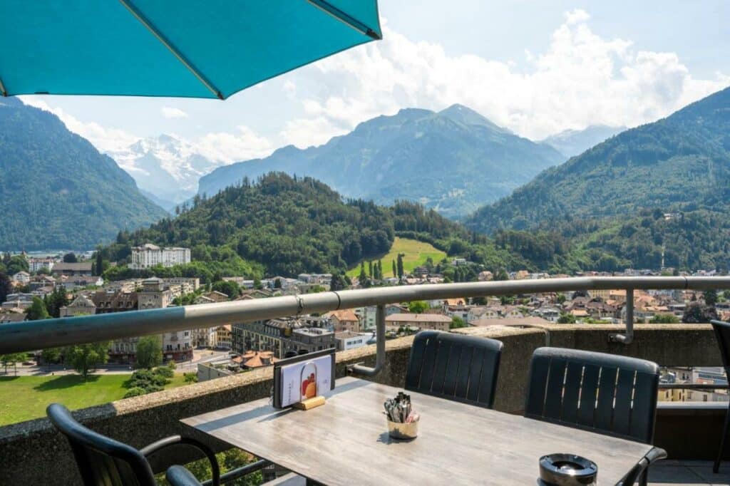 Varanda do Metropole Swiss Quality Hotel, com mesa e cadeiras e vista para a cidade e as montanhas.