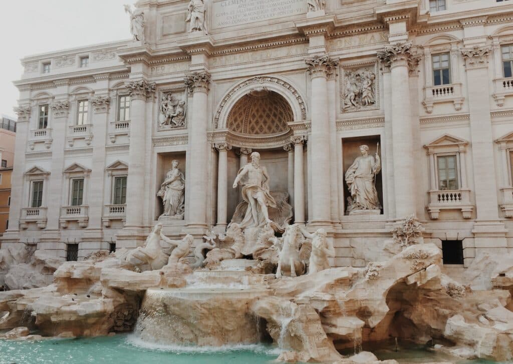 vista da fachada com colunas da Fontana di Trevi, em Roma, com águas claras e esculturas de Neptuno em estilo clássico, em branco