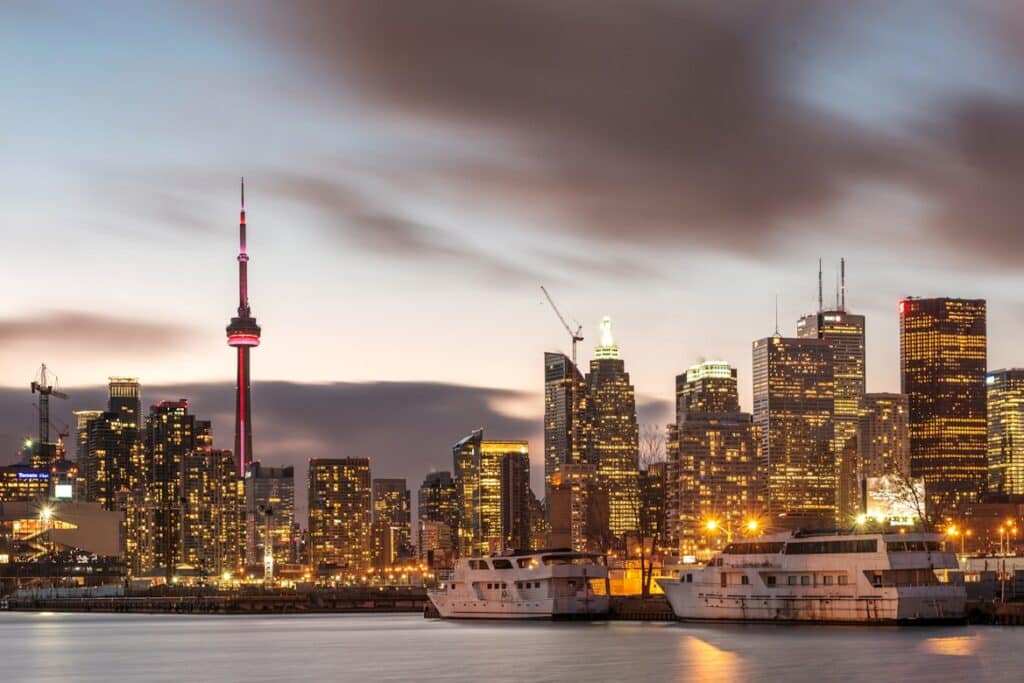 CN Tower, arranha-céus e barcos no porto iluminados ao anoitecer no centro urbano moderno de Toronto, Canadá