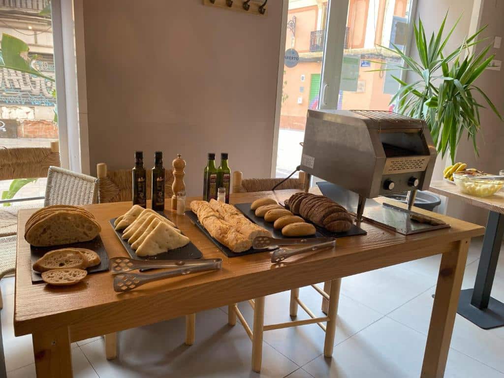 Variedade de pães artesanais, azeites e condimentos numa bancada de madeira, com forno a lenha ao fundo, num ambiente acolhedor de café do YOU &amp; CO. Quart Boutique.