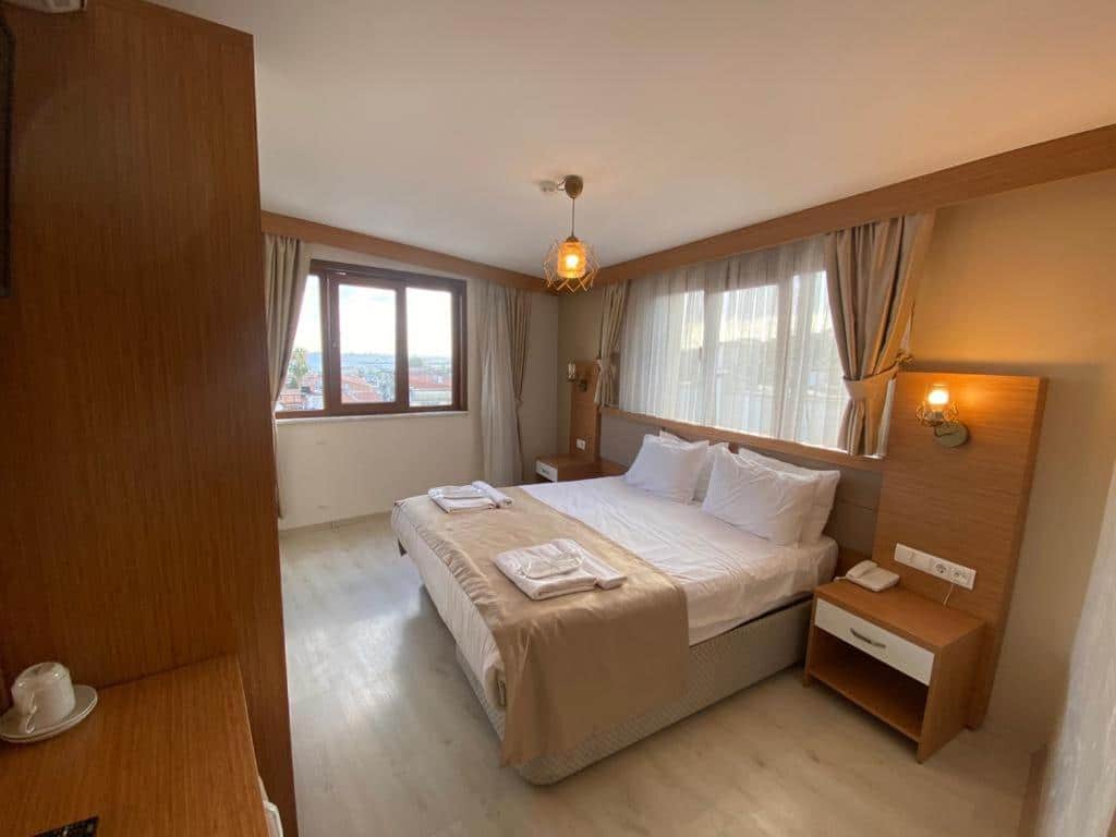 Quarto do Zeyn Otel Istanbul com uma cama de casal, duas mesas de cabeceira, uma janela com cortinas e toalhas bem dobradas sobre a cama.