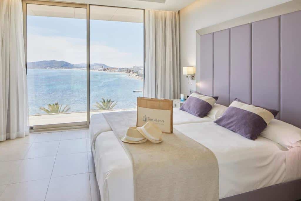 Quarto do Hotel Torre del Mar com camas individuais, cabeceira roxa e vista para o mar através de grandes janelas.