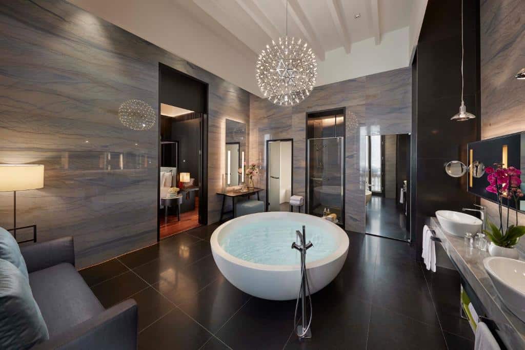 Casa de banho ampla do Mandarin Oriental, Milan com banheira de hidromassagem ao centro, sofá, candeeiro de teto, lavatórios duplos e espelho