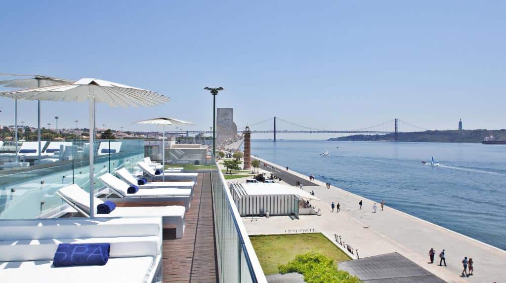Terraço do Altis Belem Hotel & Spa com piscina, espreguiçadeiras e chapéus de sol, com vista para o rio Tejo