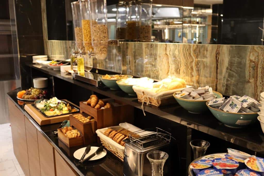 Um buffet de pequeno-almoço do Silver Crown Hotel &amp; Residence com cereais, pães, bolos, fruta, pastas e iogurte dispostos numa bancada preta.