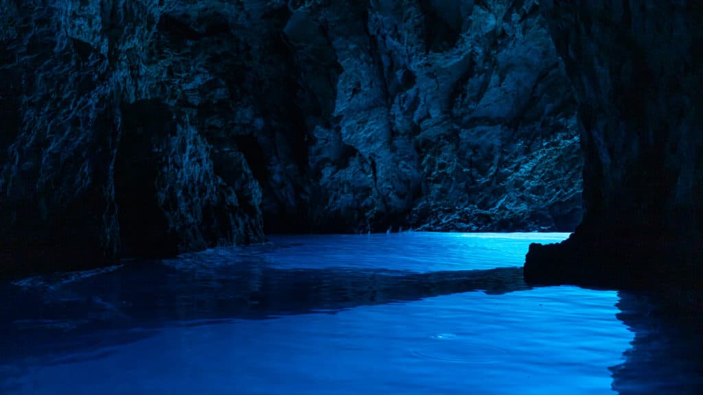 Interior da Gruta Azul, na Croácia, com uma luz fluorescente a refletir-se na água azul.