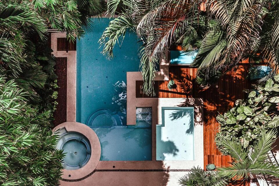Piscina azul-turquesa rodeada por palmeiras tropicais e deck de madeira no Fabiola Condo Hotel.