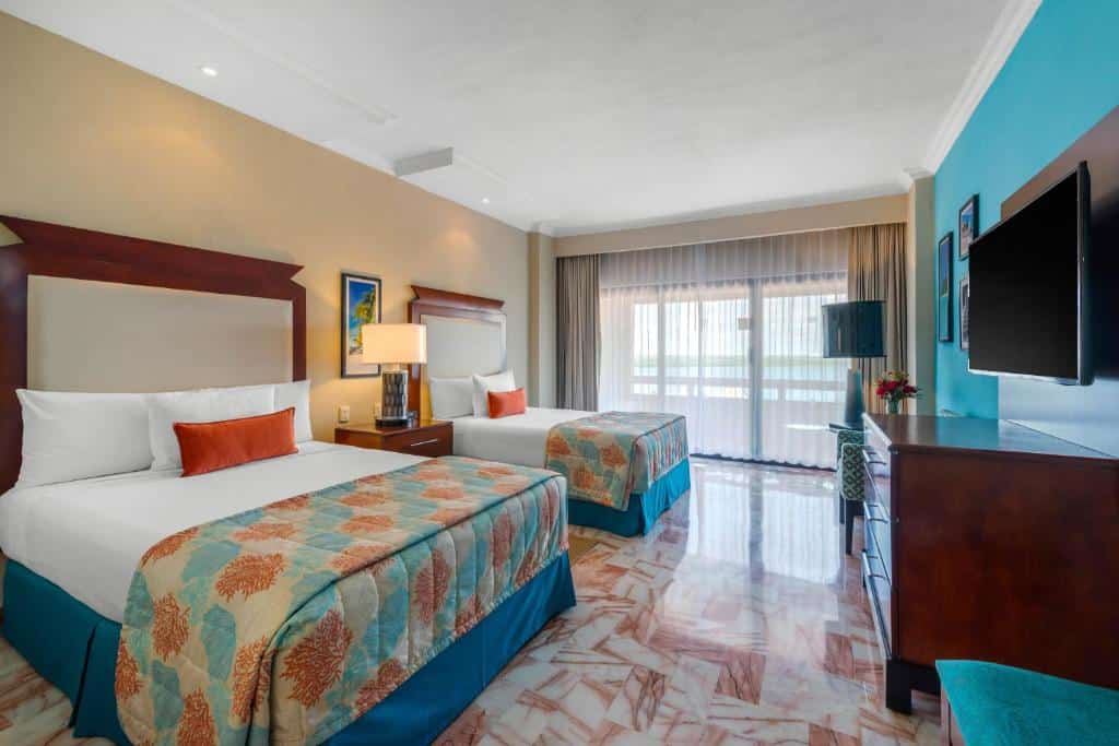 Quarto no Omni Cancun Hotel & Villas All Inclusive com cama de casal, cama de solteiro, varanda ampla e televisão, decorado em azul, branco e laranja