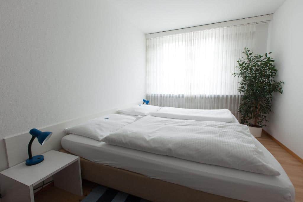 Quarto do Hotel Alpha, em Lucerna, com cama de casal e janela com cortinas brancas.