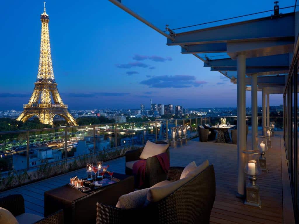 Terraço do Shangri-La Paris ao ar livre ao anoitecer, com vista para a Torre Eiffel iluminada e os edifícios da cidade ao fundo. Este é um dos hotéis de luxo em Paris.