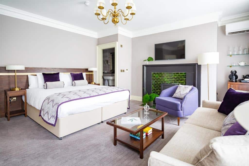 Quarto do Trinity Townhouse Hotel com cama king size, decoração elegante em tons de roxo e cinzento, lareira a gás, televisão de ecrã grande e poltrona confortável.