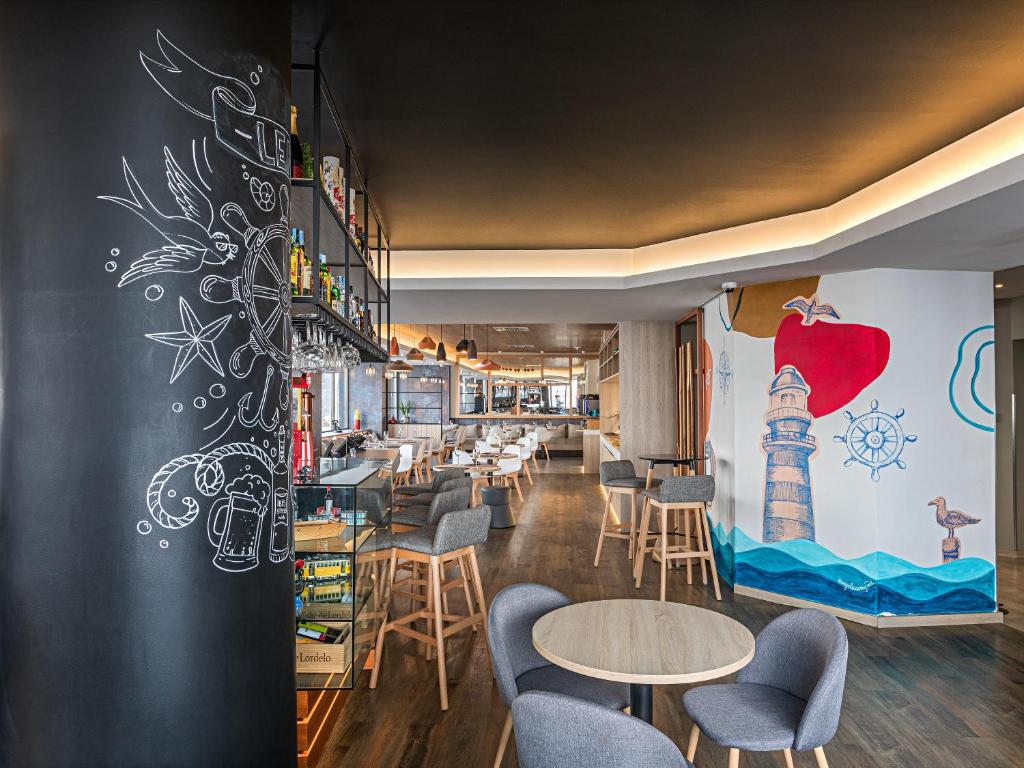 Área de refeições do Hotel Ibis Styles Lisboa Liberdade com mesas redondas, cadeiras estofadas em cinzento e paredes com desenhos pintados que remetem para o mar