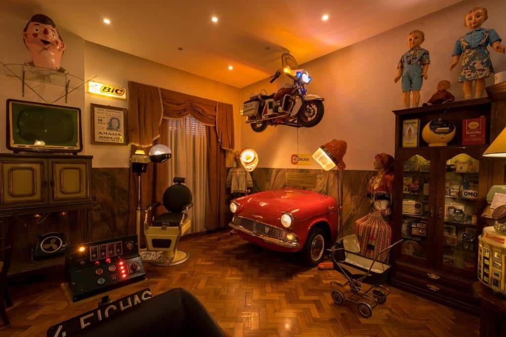 Sala repleta de peças vintage, incluindo um automóvel vermelho, uma TV antiga, brinquedos, uma cadeira de barbeiro e uma mota na parede, no Pão de Açúcar Hotel.