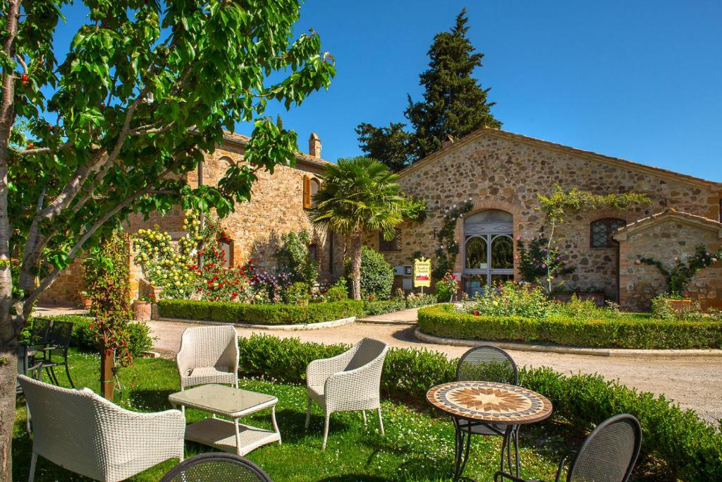 Área exterior do Castello di Spedaletto da Laura, um dos hotéis na Toscana, com vários jardins floridos, relva verde, cadeiras espalhadas no meio da natureza, céu azul e entrada do edifício