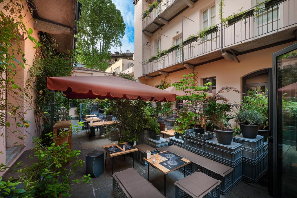 Terraço partilhado do Maison Borella com vasos de plantas, mesas e bancos de madeira e um toldo vermelho