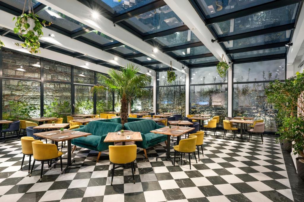 Um restaurante do Monastery Boutique Hotel com pavimento xadrez, cadeiras amarelas, sofás verdes, teto de vidro e plantas por todo o espaço.