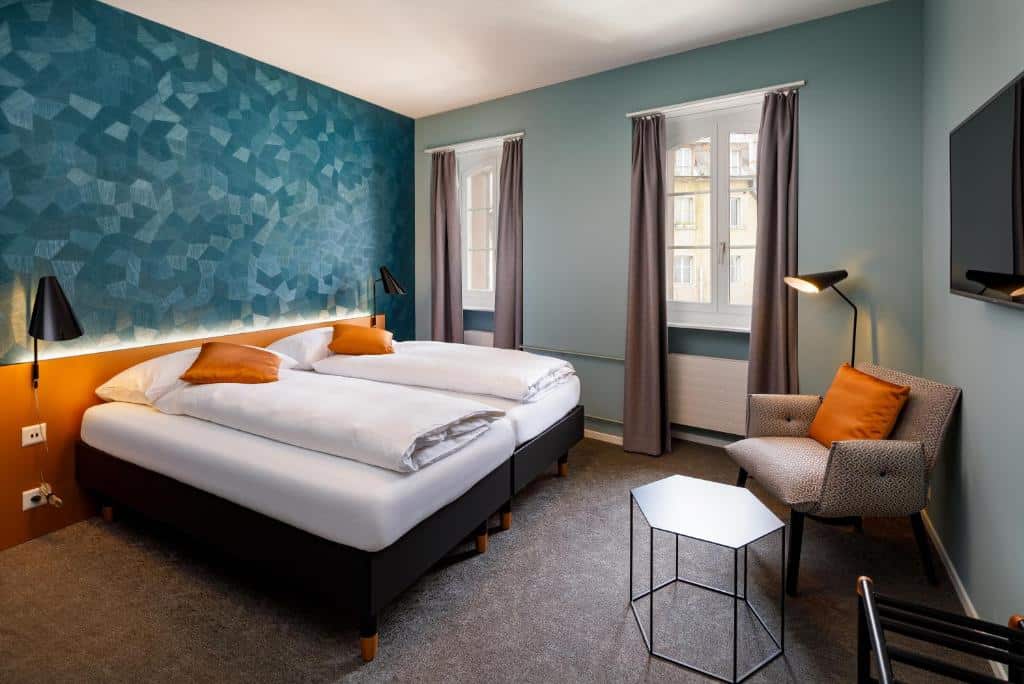 Quarto do Hotel Münzgasse, com cama de casal, duas janelas, poltrona e televisão.