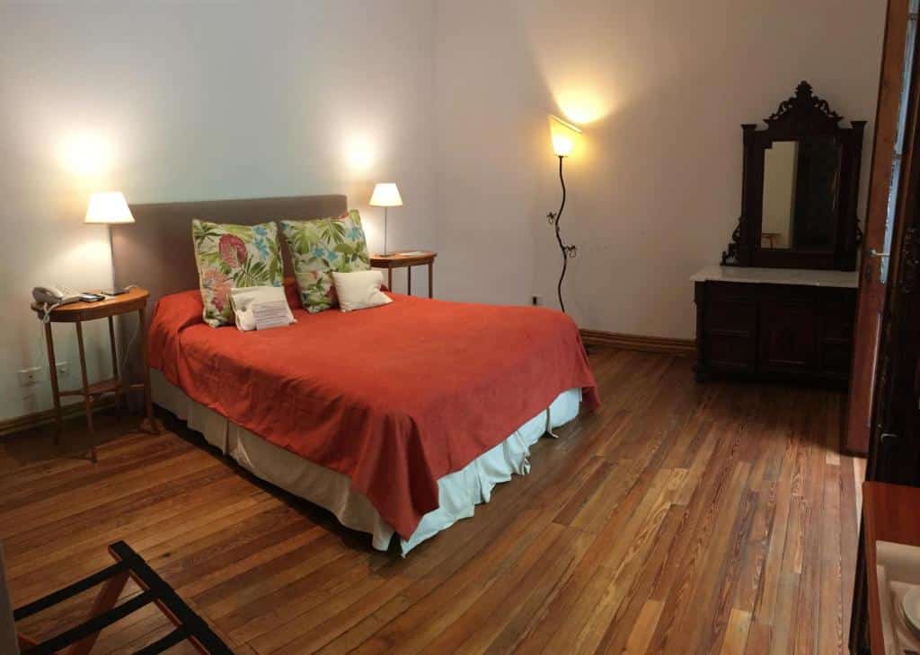 quarto do Cruce´s Hotel Boutique com cama de casal em tons terrosos, mesas e candeeiros dos dois lados, uma cómoda e um espelho de madeira