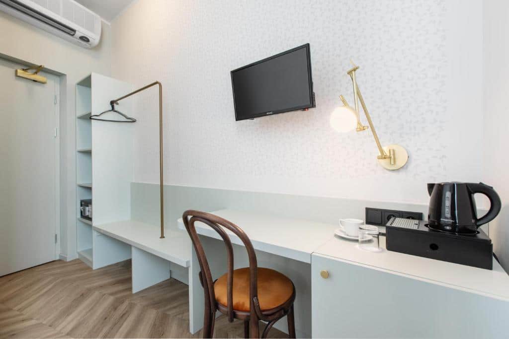 Zona de trabalho minimalista de um quarto do Hotel Beránek, com uma cadeira, TV na parede, jarro elétrico, chávenas, prateleira e cabide.