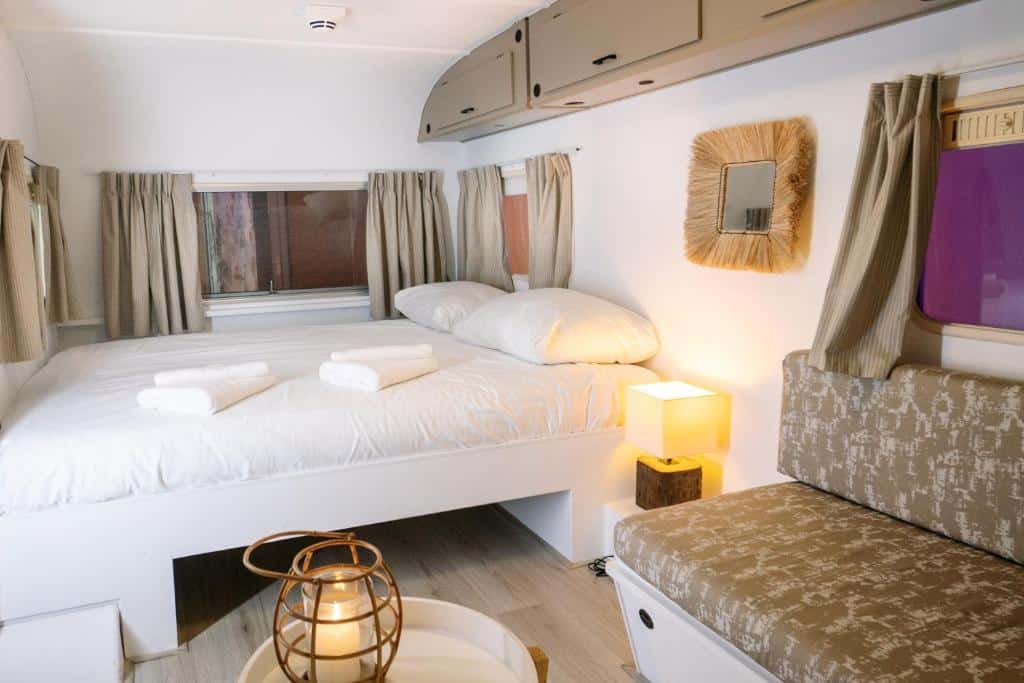 Interior da caravana vintage do Outside Inn, de 7 m², com cama de casal, um sofá e uma mesinha de centro com candeeiro, e armário suspenso na parede