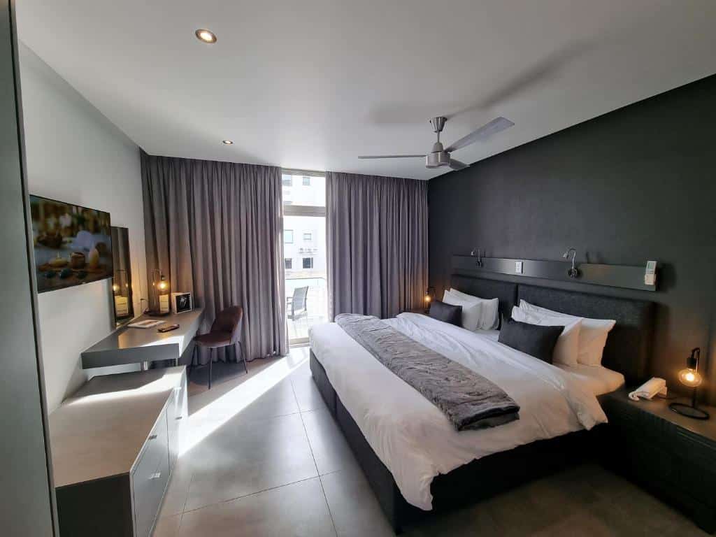 Quarto do Atlantic Affair Boutique Hotel com cama grande, secretária, TV, cortinas cinzentas, ventoinha de teto e luz natural.