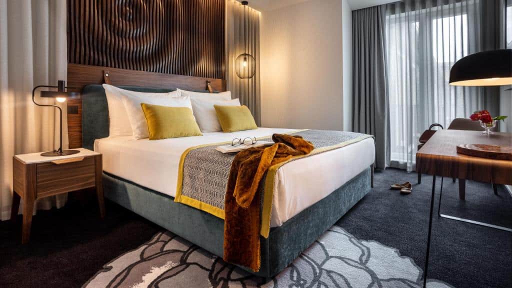 Quarto da Pousada do Porto – Rua das Flores, com cama de casal à esquerda, uma cómoda com candeeiro e uma mesa de madeira em frente.