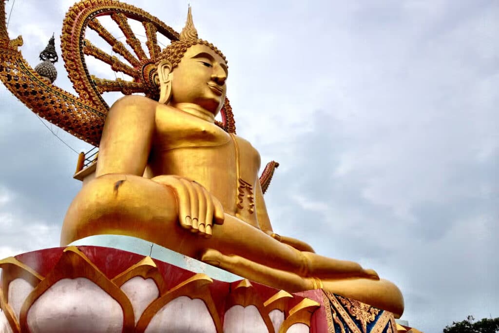 Grande estátua dourada do Buda sentado ao ar livre, com detalhes ornamentados, no templo Wat Phra Yai, em Koh Samui.