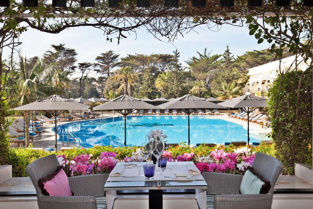 Piscina do Palácio Estoril Hotel rodeada de árvores e flores, com mesa posta com taças e velas