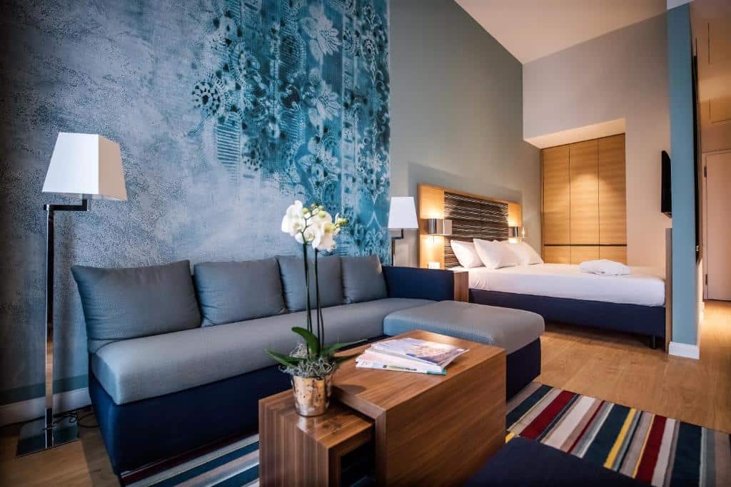 Quarto do The Wellem com sala de estar, sofá, mesa de centro e cama de casal ao fundo. Representa hotéis em Dusseldorf.