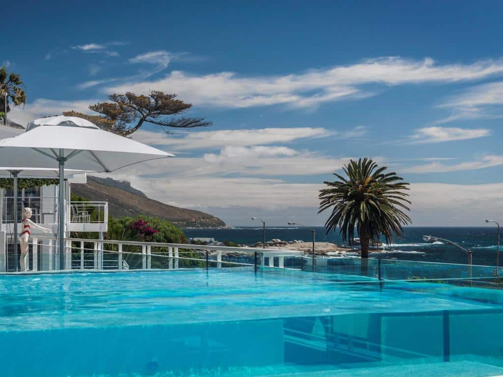 Piscina exterior no South Beach Camps Bay Boutique Hotel com um chapéu de sol branco e vista para o oceano e palmeiras.