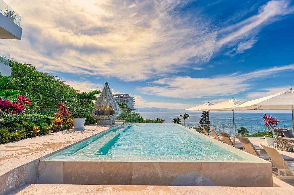 Piscina infinita das Maxwell Residences at Indah com espreguiçadeiras e chapéus de sol com vista para o oceano, rodeada de plantas tropicais.