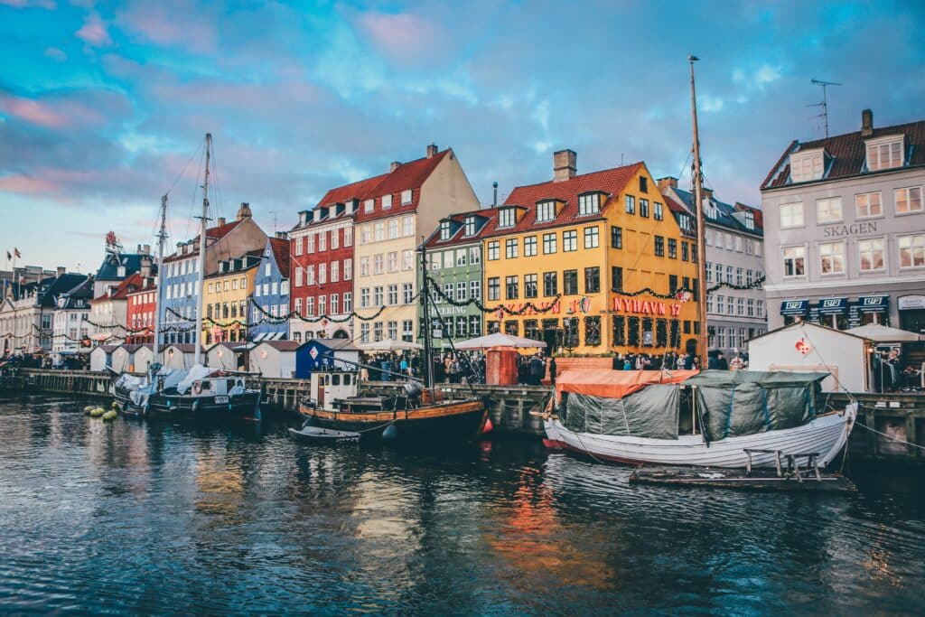 Canal de Nyhavn em Copenhaga. Na foto há vários barcos ancorados e edifícios coloridos ao longo da margem.